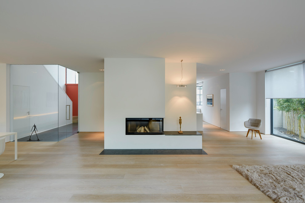 Modelo de salón abierto contemporáneo extra grande con chimenea lineal, paredes blancas, suelo de madera clara y marco de chimenea de yeso