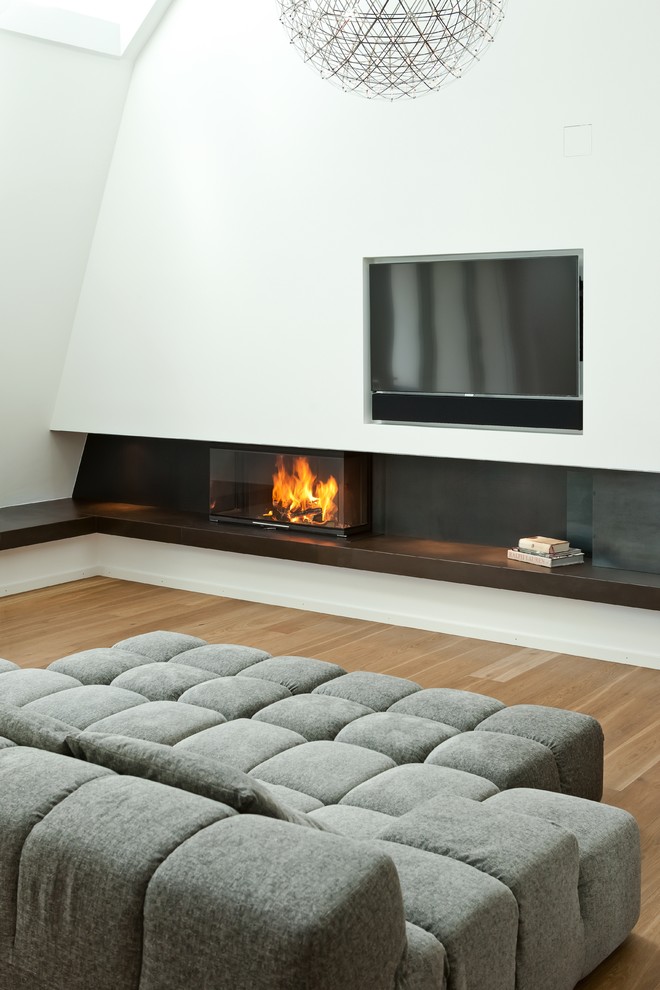 Inspiration for a mid-sized contemporary formal and enclosed medium tone wood floor and brown floor living room remodel in Munich with white walls, a wood stove, a stone fireplace and a wall-mounted tv