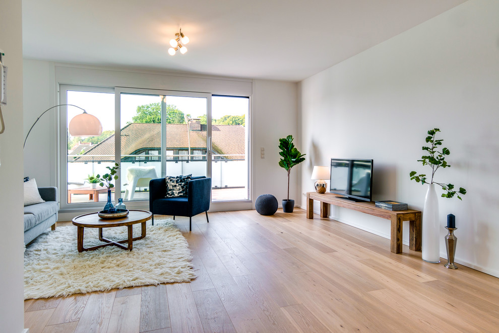 Großes, Offenes Skandinavisches Wohnzimmer ohne Kamin mit weißer Wandfarbe, braunem Holzboden, freistehendem TV und braunem Boden in Hamburg