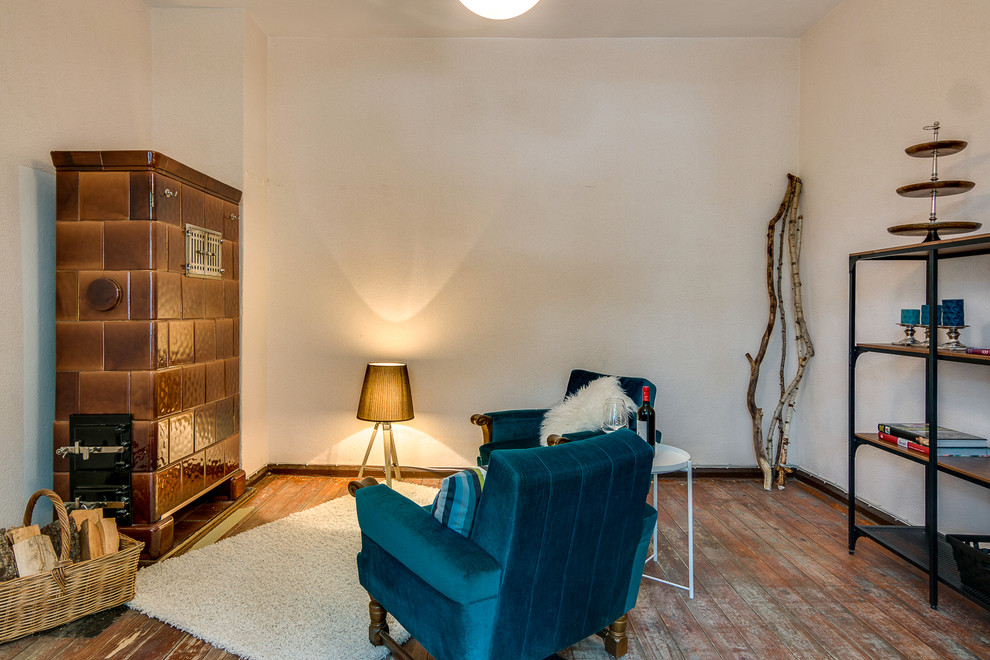 Cette image montre un petit salon bohème fermé avec un mur blanc, un sol en bois brun, un poêle à bois, un manteau de cheminée en carrelage, aucun téléviseur et un sol marron.