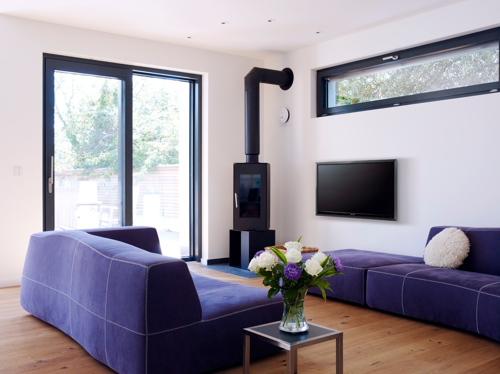 Идея дизайна: парадная гостиная комната среднего размера в современном стиле с белыми стенами, паркетным полом среднего тона, печью-буржуйкой и телевизором на стене
