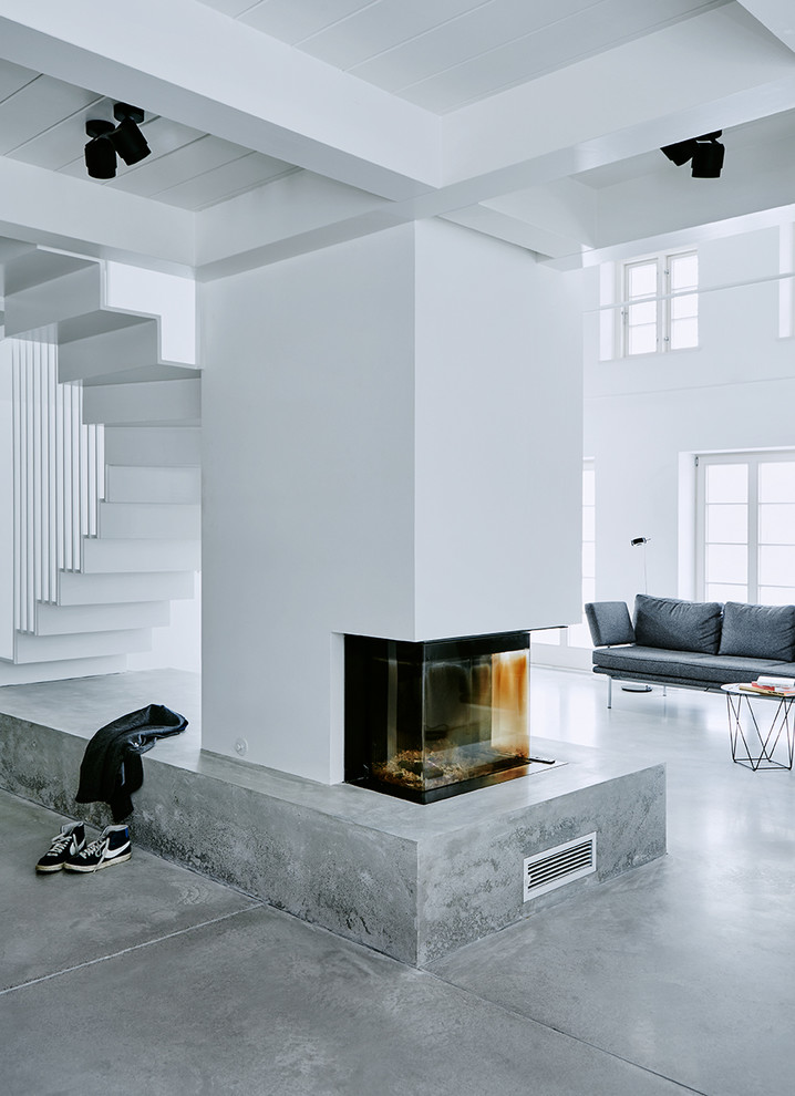 Cette image montre un grand salon design ouvert avec un mur blanc, sol en béton ciré et un manteau de cheminée en plâtre.