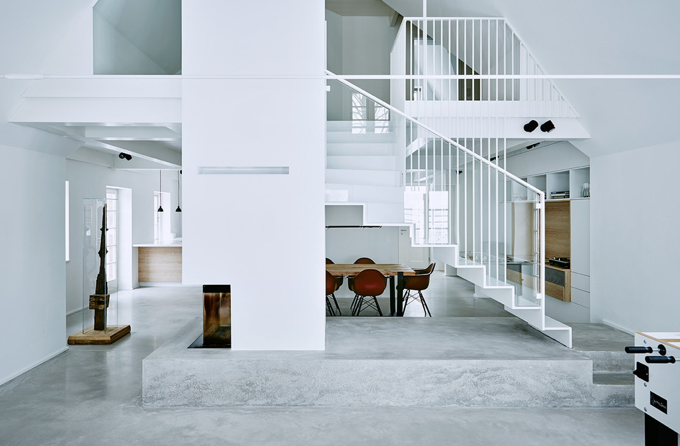 Réalisation d'un grand salon design ouvert avec un mur blanc, sol en béton ciré, un manteau de cheminée en plâtre et une cheminée d'angle.