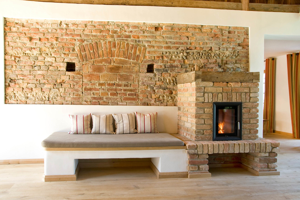 This is an example of a farmhouse living room in Munich with white walls, a standard fireplace and a brick fireplace surround.