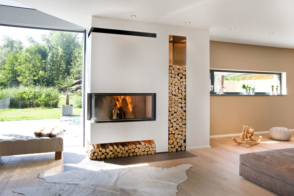 Foto de sala de estar abierta contemporánea con paredes beige, chimenea de esquina, marco de chimenea de yeso y suelo de madera clara