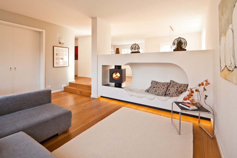 Exemple d'une salle de séjour moderne de taille moyenne et fermée avec un mur blanc, parquet clair, cheminée suspendue, un manteau de cheminée en plâtre et un sol beige.