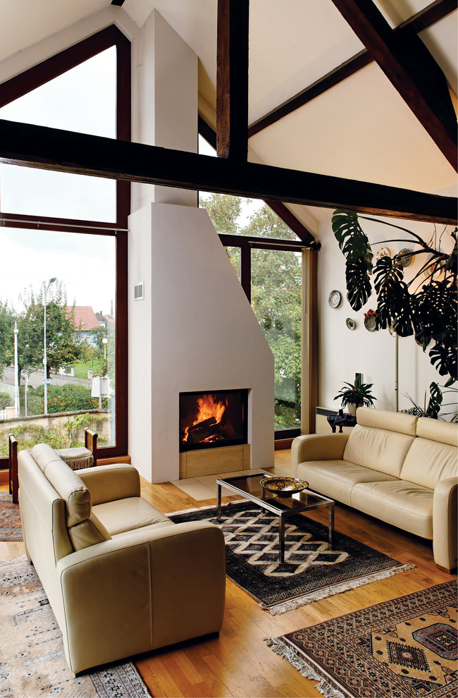 Réalisation d'un salon design avec un mur blanc, un sol en bois brun, une cheminée standard et un manteau de cheminée en plâtre.