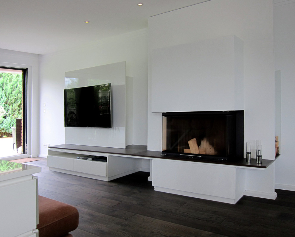 Inspiration for a medium sized contemporary open plan games room in Cologne with white walls, dark hardwood flooring, a standard fireplace, a plastered fireplace surround and a built-in media unit.