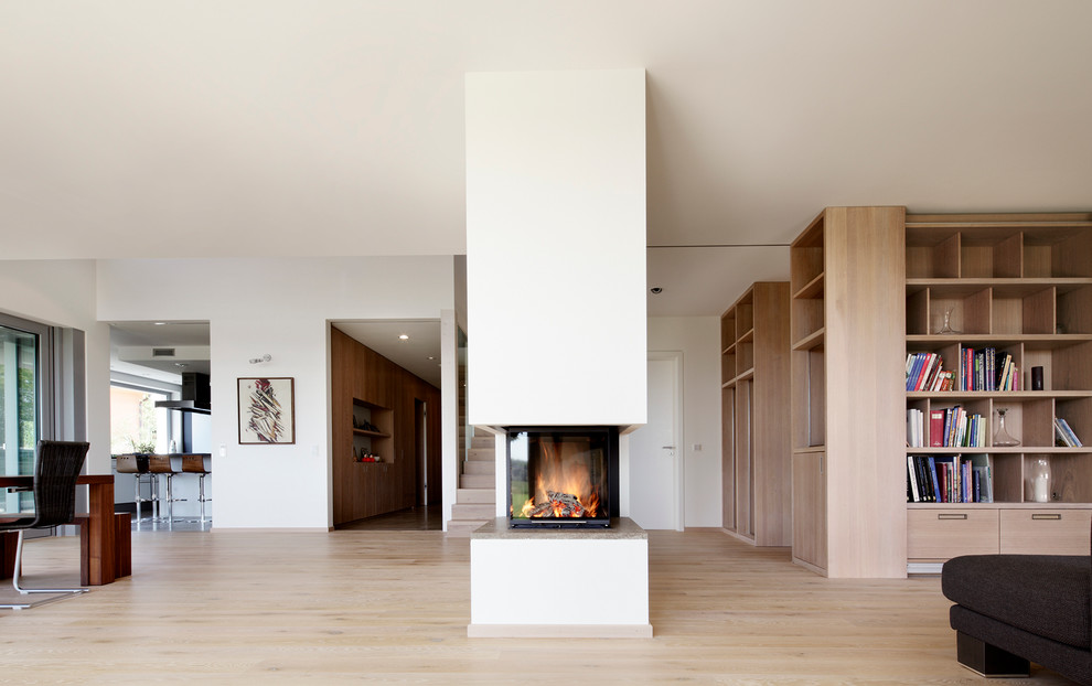 Cette image montre un grand salon minimaliste ouvert avec une cheminée double-face, un mur blanc, parquet clair et un manteau de cheminée en plâtre.