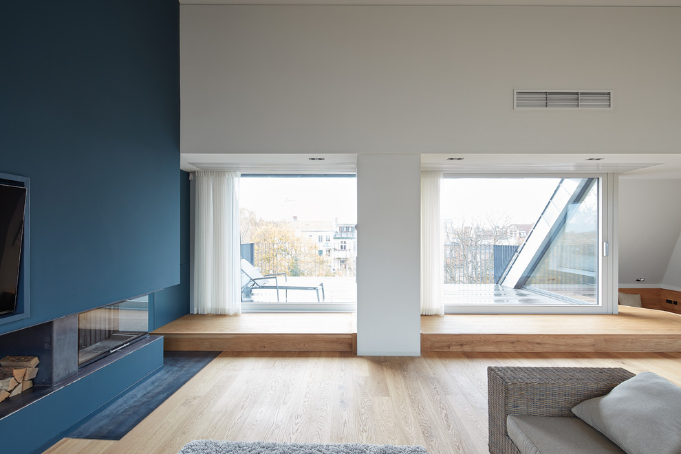 Cette image montre une grande salle de séjour design ouverte avec un mur bleu, salle de jeu, parquet clair, un poêle à bois, un téléviseur fixé au mur et un sol beige.