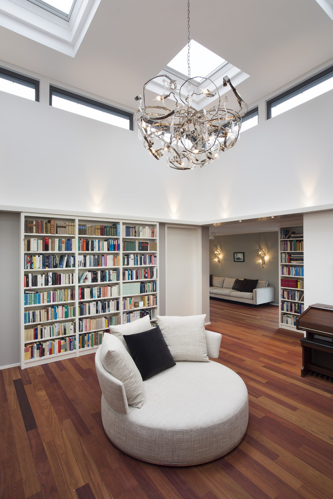 Réalisation d'un grand salon design ouvert avec une bibliothèque ou un coin lecture, un mur blanc et un sol en bois brun.