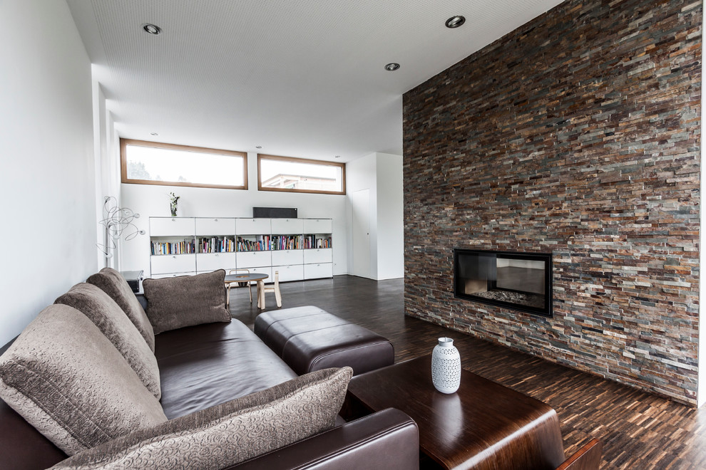 Offenes Modernes Wohnzimmer mit weißer Wandfarbe, dunklem Holzboden, Tunnelkamin und Kaminumrandung aus Stein in Sonstige