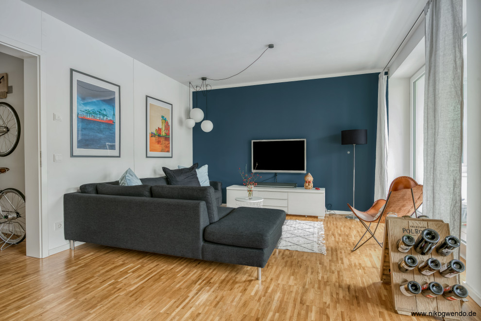 Modelo de sala de estar abierta marinera de tamaño medio con paredes azules, suelo de madera clara y televisor colgado en la pared