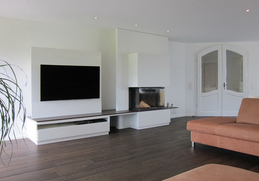 Imagen de sala de estar abierta contemporánea de tamaño medio con paredes blancas, suelo de madera oscura, todas las chimeneas, marco de chimenea de yeso y pared multimedia
