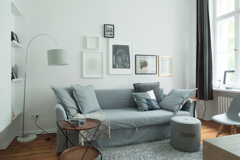 Modelo de sala de estar tipo loft nórdica pequeña sin chimenea y televisor con paredes blancas, suelo laminado y suelo marrón