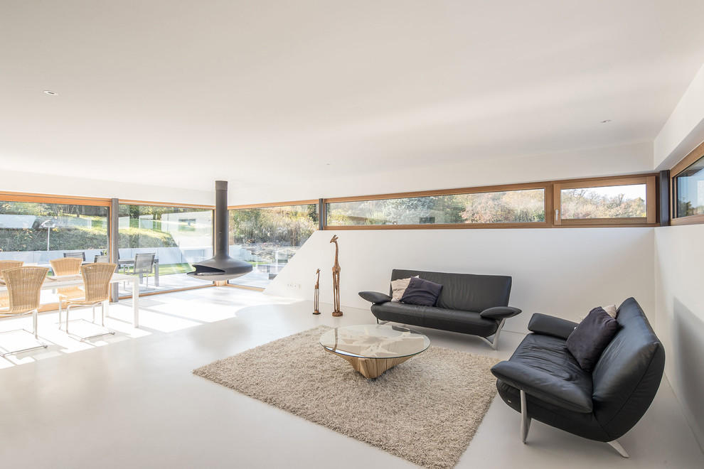 Offenes Modernes Wohnzimmer mit weißer Wandfarbe, Betonboden, Hängekamin und grauem Boden in Sonstige