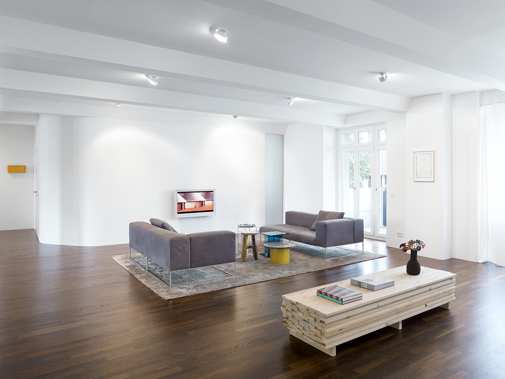 Photo of a large contemporary formal living room in Berlin with white walls, medium hardwood flooring, a wall mounted tv and no fireplace.