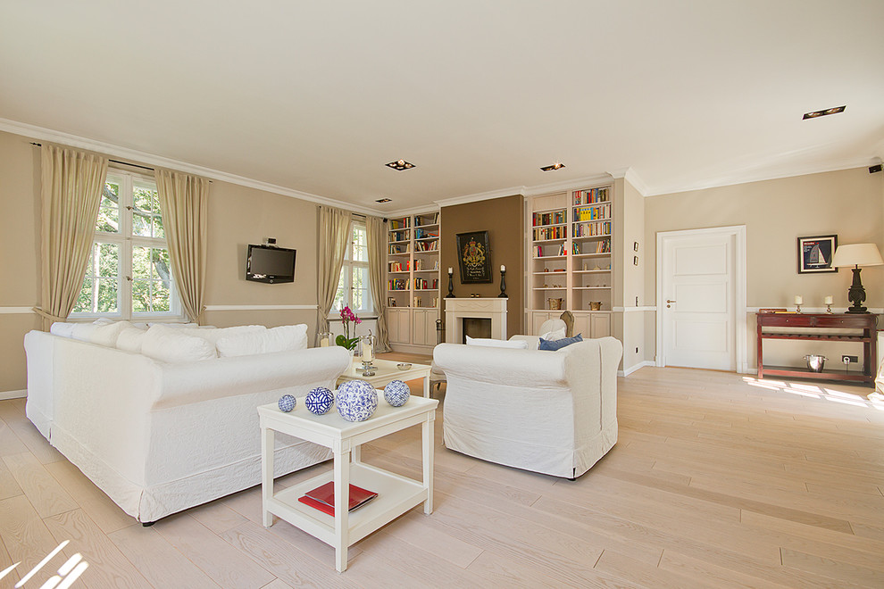 Immagine di un ampio soggiorno design aperto con libreria, pareti beige, parquet chiaro, camino classico e TV a parete