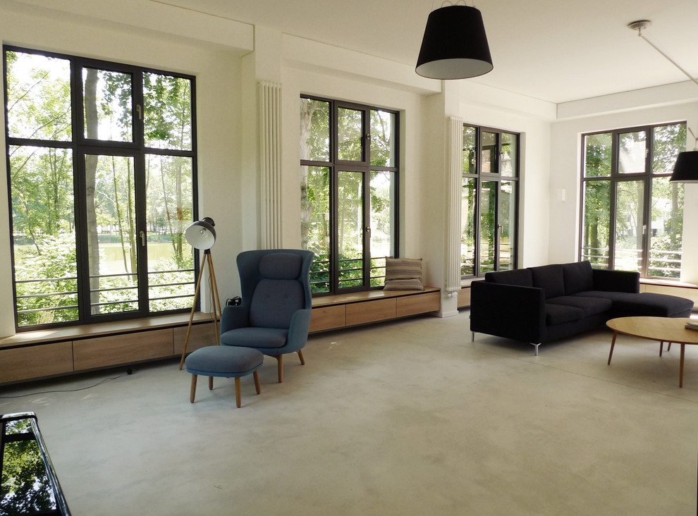 На фото: большая гостиная комната в современном стиле с белыми стенами и бетонным полом без камина