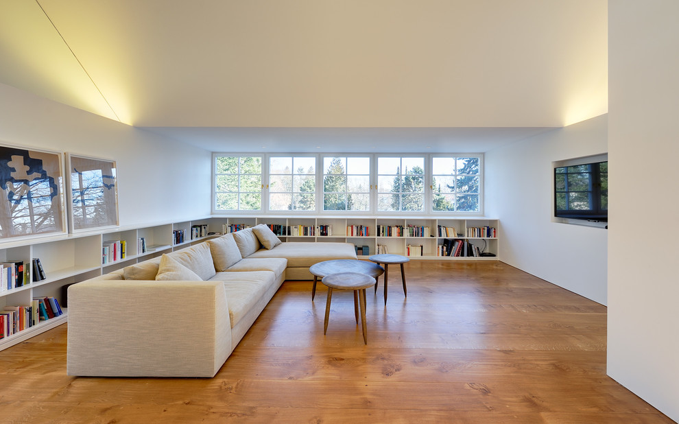 Exemple d'un grand salon tendance ouvert avec un sol en bois brun, un téléviseur fixé au mur, une bibliothèque ou un coin lecture, un mur blanc et aucune cheminée.