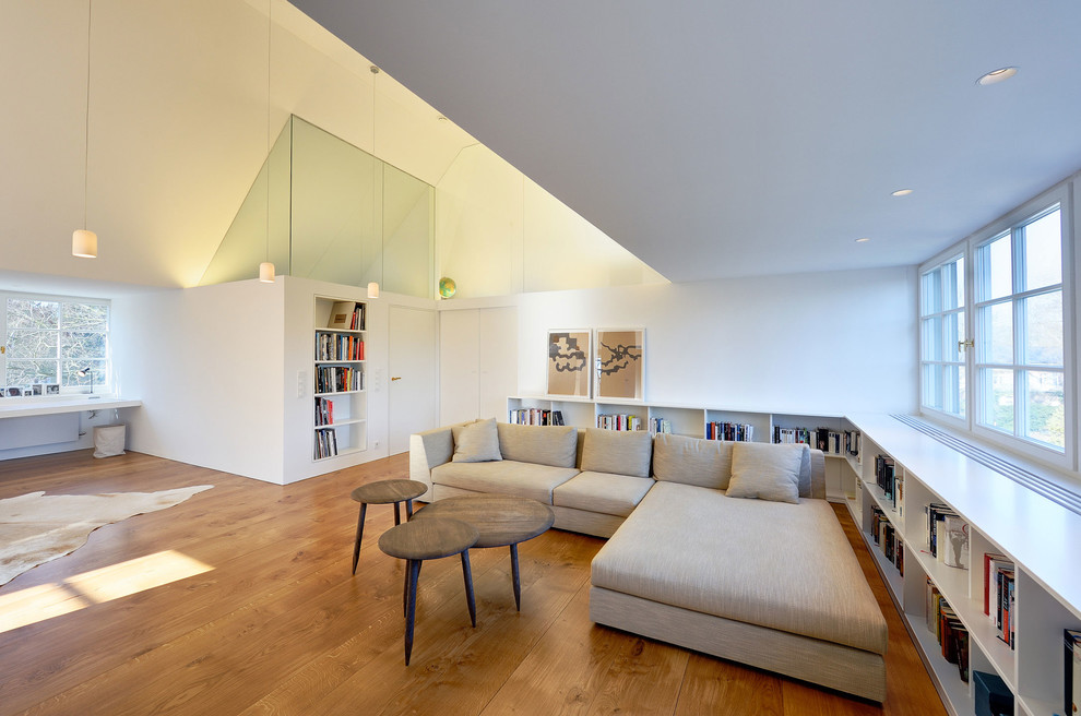 Foto på ett stort funkis allrum med öppen planlösning, med ett bibliotek, vita väggar och mellanmörkt trägolv