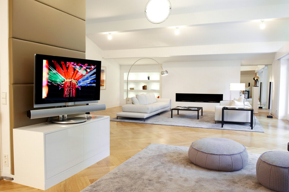 Expansive contemporary open plan games room in Munich with white walls, a ribbon fireplace, a freestanding tv and light hardwood flooring.