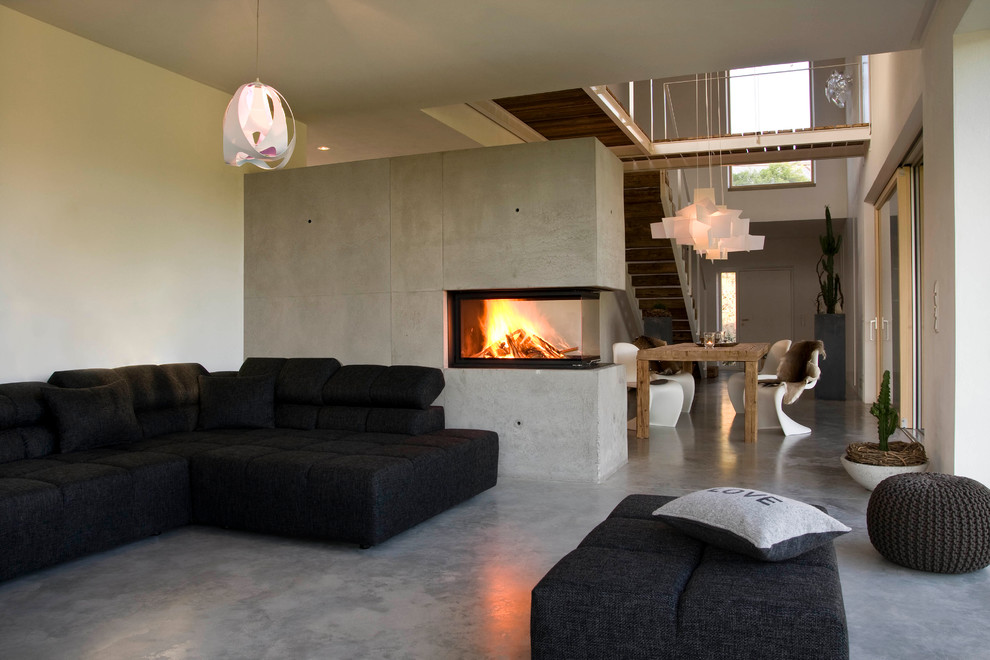 Ejemplo de salón abierto y cemento moderno grande con paredes blancas, suelo de cemento, marco de chimenea de hormigón, chimenea de esquina y suelo gris