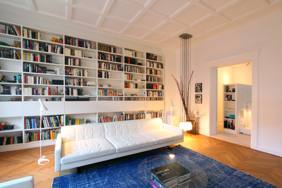 Modelo de sala de estar con biblioteca cerrada nórdica grande sin televisor y chimenea con paredes blancas y suelo de madera en tonos medios
