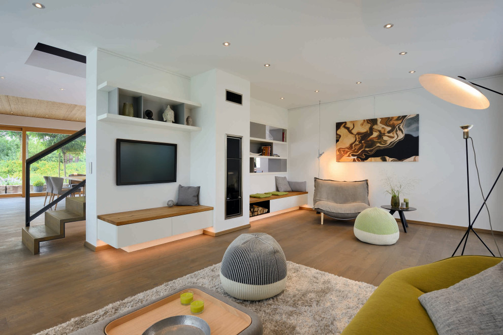 Стильный дизайн: открытая гостиная комната в современном стиле с белыми стенами, паркетным полом среднего тона, телевизором на стене и коричневым полом - последний тренд