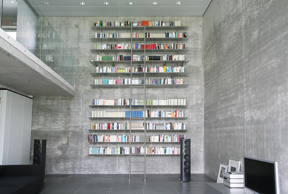 Exempel på ett stort industriellt allrum med öppen planlösning, med ett bibliotek, grå väggar och en fristående TV