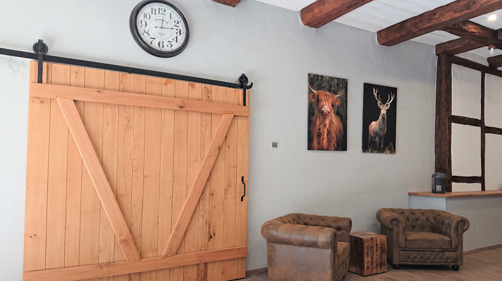 Geräumiges Country Wohnzimmer im Loft-Stil mit grauer Wandfarbe, Vinylboden, braunem Boden, freigelegten Dachbalken und Holzwänden in Hannover