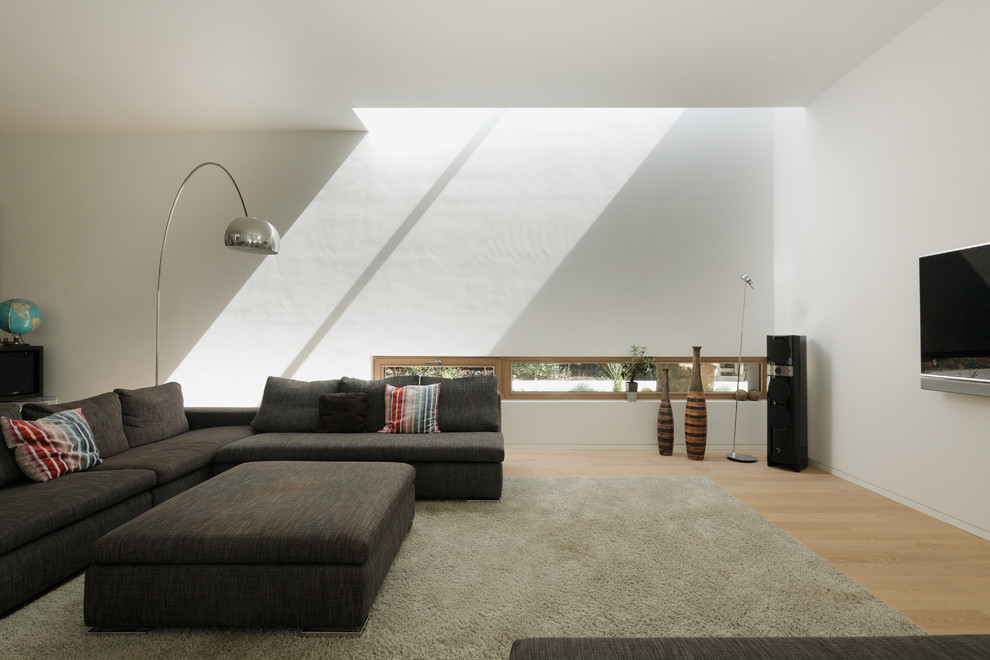 На фото: большая открытая гостиная комната в современном стиле с белыми стенами, светлым паркетным полом и телевизором на стене