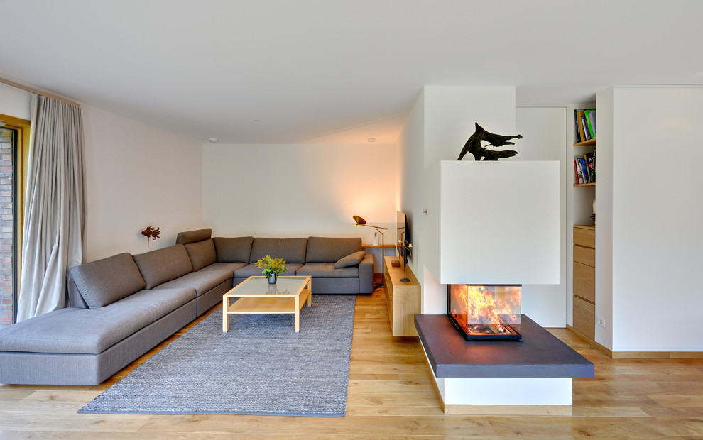 Design ideas for a large contemporary open plan games room in Berlin with white walls, medium hardwood flooring, a wall mounted tv, a two-sided fireplace and a plastered fireplace surround.