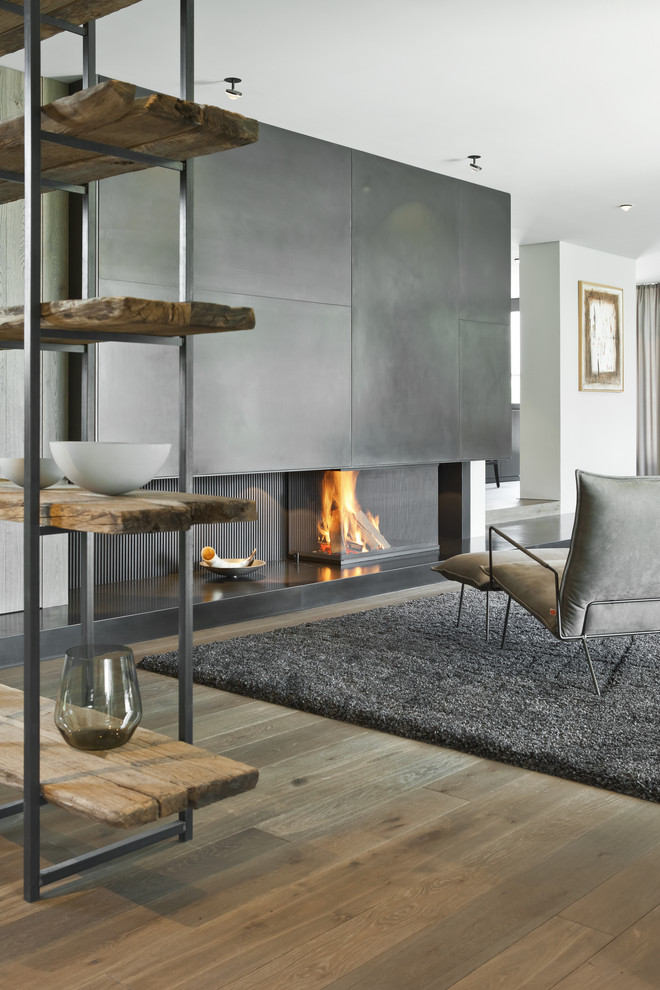 Immagine di un ampio soggiorno design aperto con pareti bianche, pavimento in legno massello medio, stufa a legna, cornice del camino in metallo e pavimento marrone