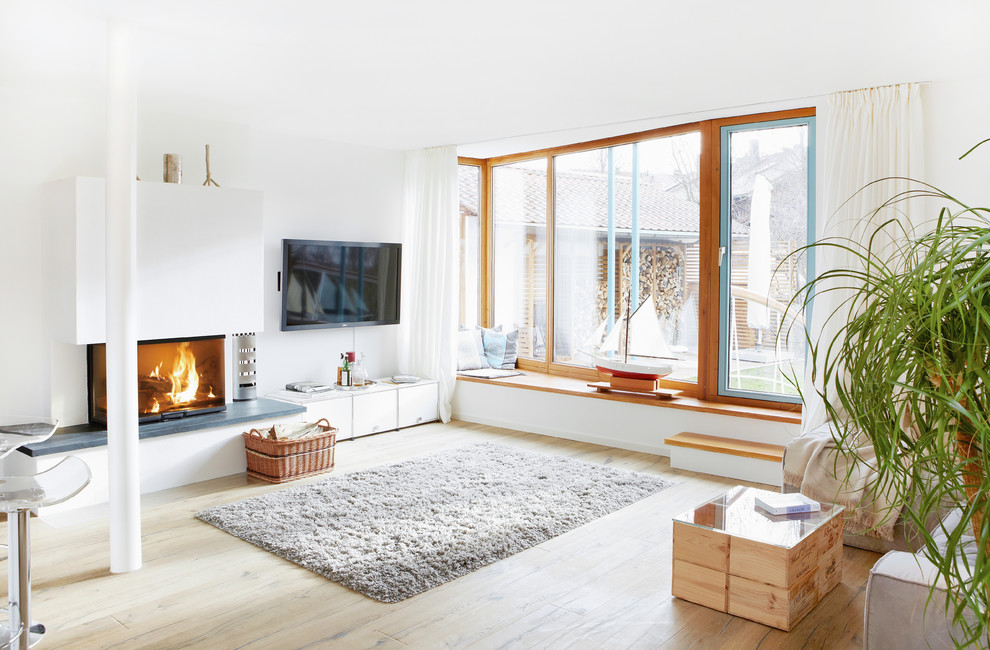 Mittelgroßes, Offenes Modernes Wohnzimmer mit weißer Wandfarbe, braunem Holzboden, Kaminumrandung aus Beton, TV-Wand und Eckkamin in München
