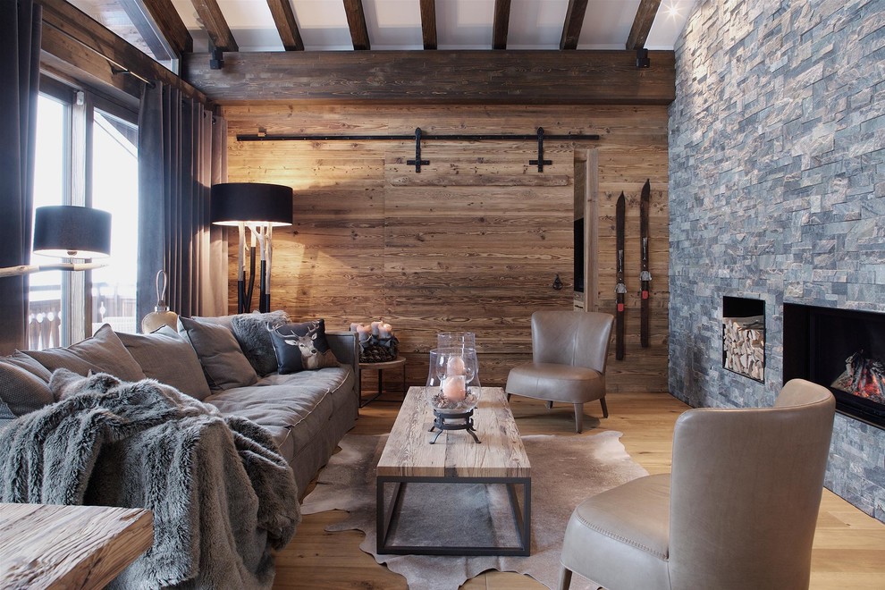 Exemple d'un salon montagne fermé avec parquet clair, une cheminée standard, un manteau de cheminée en pierre, aucun téléviseur, un mur en pierre et éclairage.