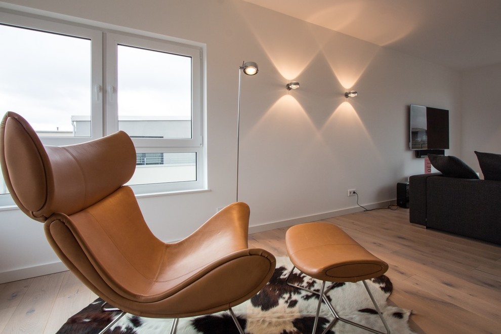Diseño de salón para visitas minimalista con paredes blancas, suelo de madera clara, televisor colgado en la pared y suelo marrón