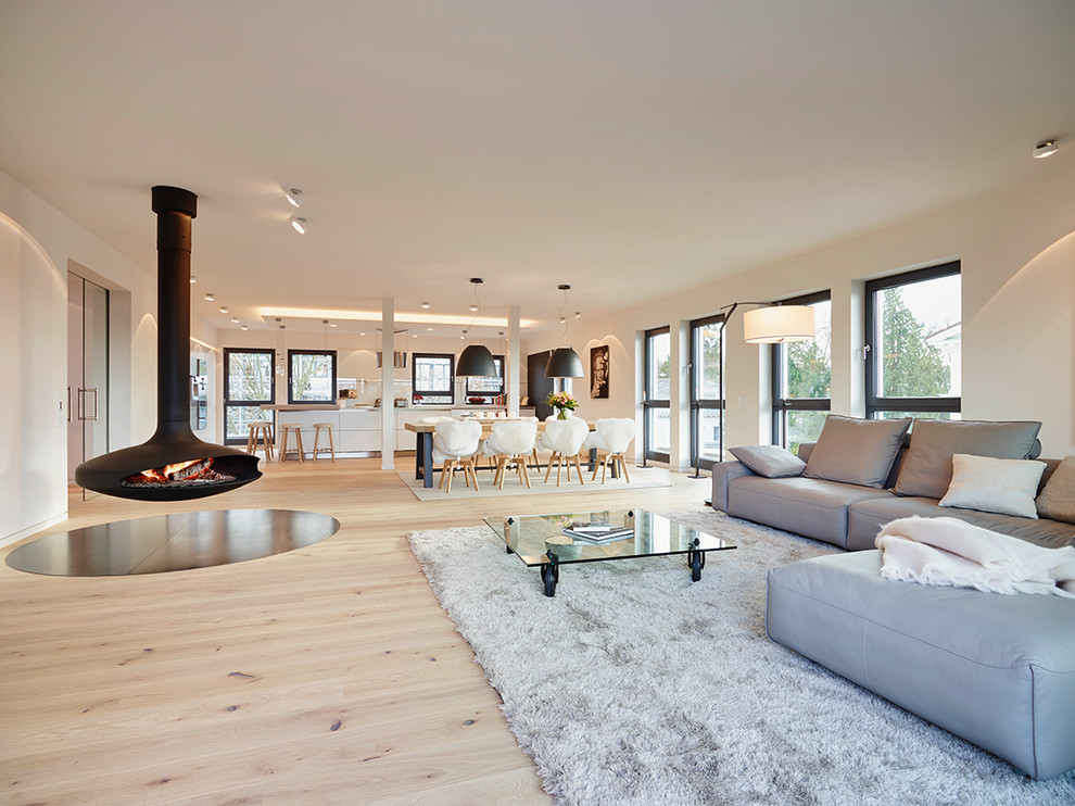 Imagen de salón abierto contemporáneo extra grande con paredes blancas, suelo de madera clara y chimeneas suspendidas