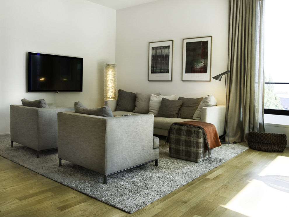 Imagen de sala de estar cerrada actual de tamaño medio sin chimenea con paredes blancas, suelo de madera clara, televisor colgado en la pared y suelo marrón