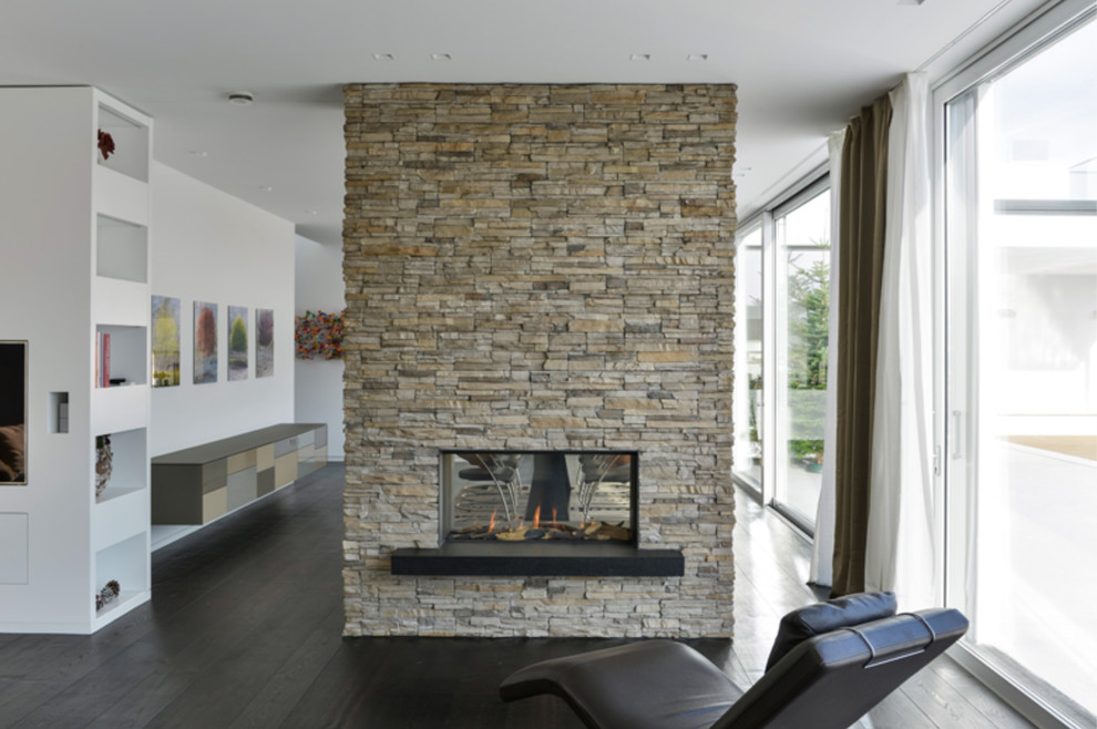 Inspiration pour un salon design avec un mur blanc, parquet foncé, une cheminée double-face et un manteau de cheminée en pierre.
