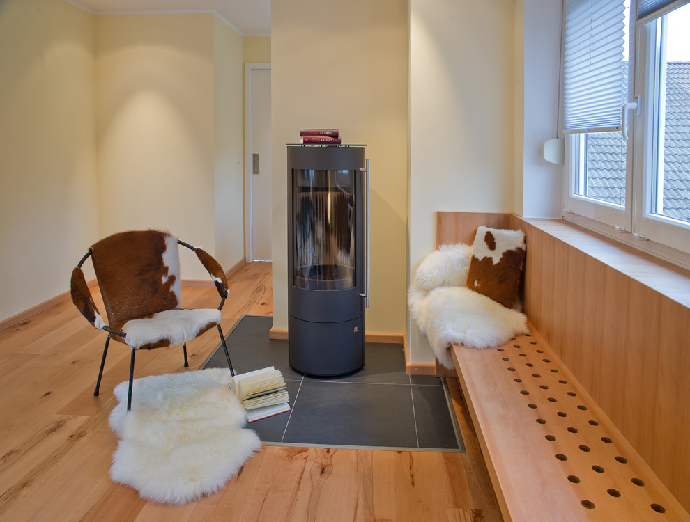 На фото: гостиная комната среднего размера в скандинавском стиле с деревянным полом, печью-буржуйкой, фасадом камина из камня и белыми стенами