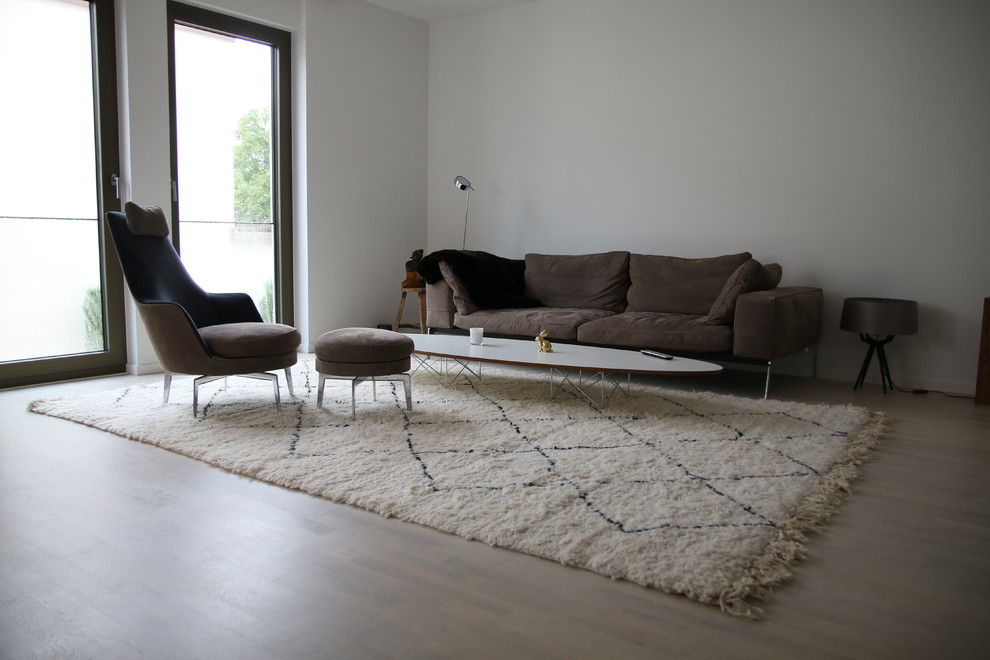Diseño de sala de estar cerrada actual de tamaño medio sin chimenea y televisor con paredes blancas, suelo de madera clara y suelo marrón