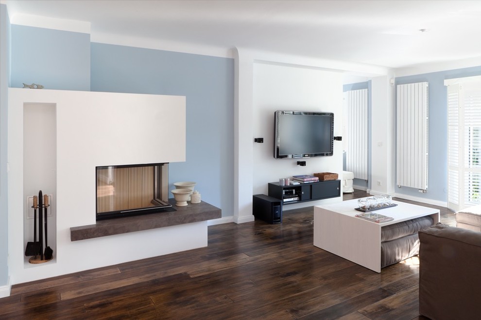 Aménagement d'une salle de séjour contemporaine ouverte avec un mur bleu, parquet foncé, une cheminée d'angle, un téléviseur fixé au mur et un manteau de cheminée en plâtre.