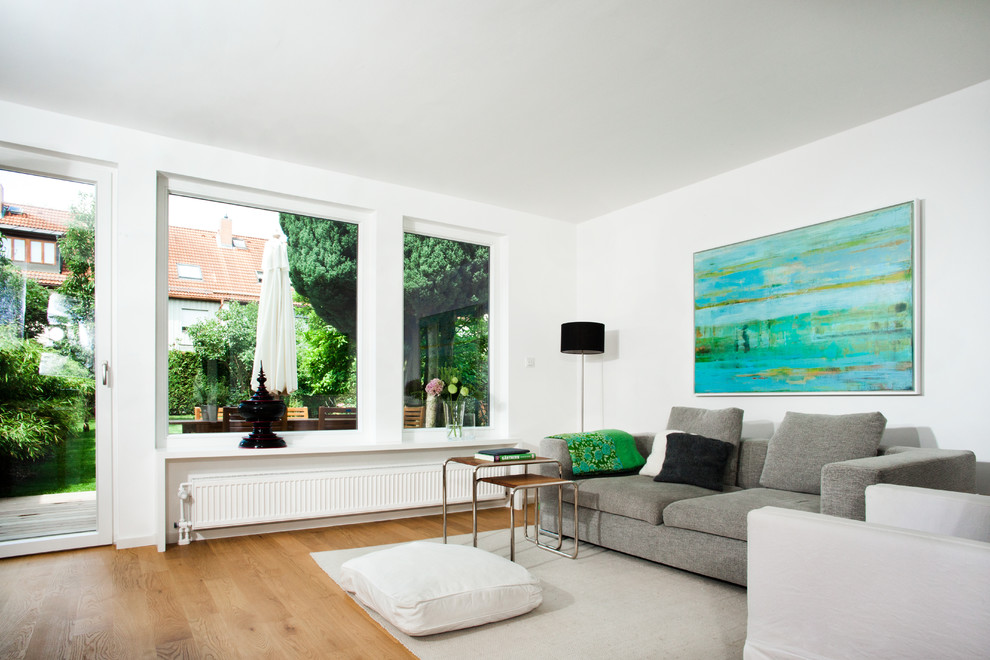 Mittelgroßes, Offenes Modernes Wohnzimmer mit weißer Wandfarbe, braunem Holzboden, Eckkamin, verputzter Kaminumrandung und TV-Wand in München