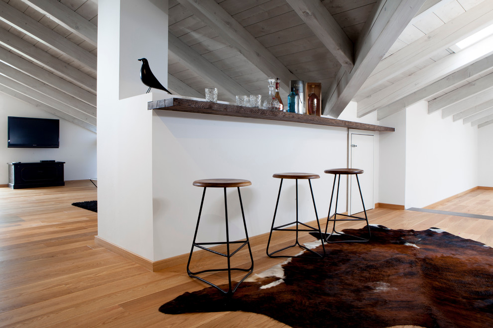 Modelo de salón con barra de bar cerrado nórdico grande con paredes blancas, suelo de madera clara, televisor colgado en la pared, estufa de leña, marco de chimenea de metal y suelo marrón