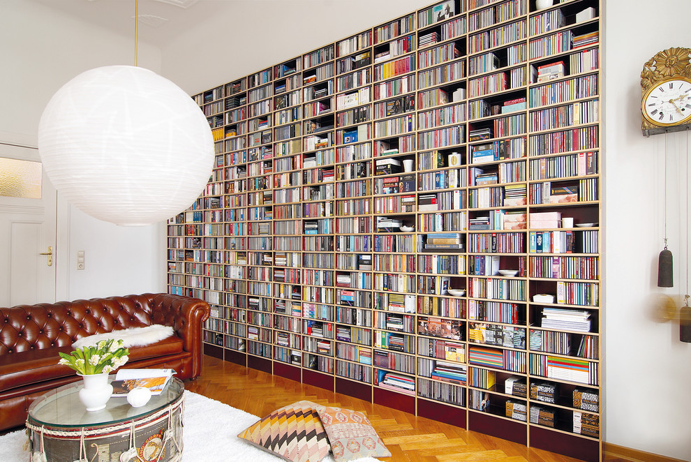 Cette image montre un grand salon design fermé avec une bibliothèque ou un coin lecture, un mur blanc et un sol en bois brun.