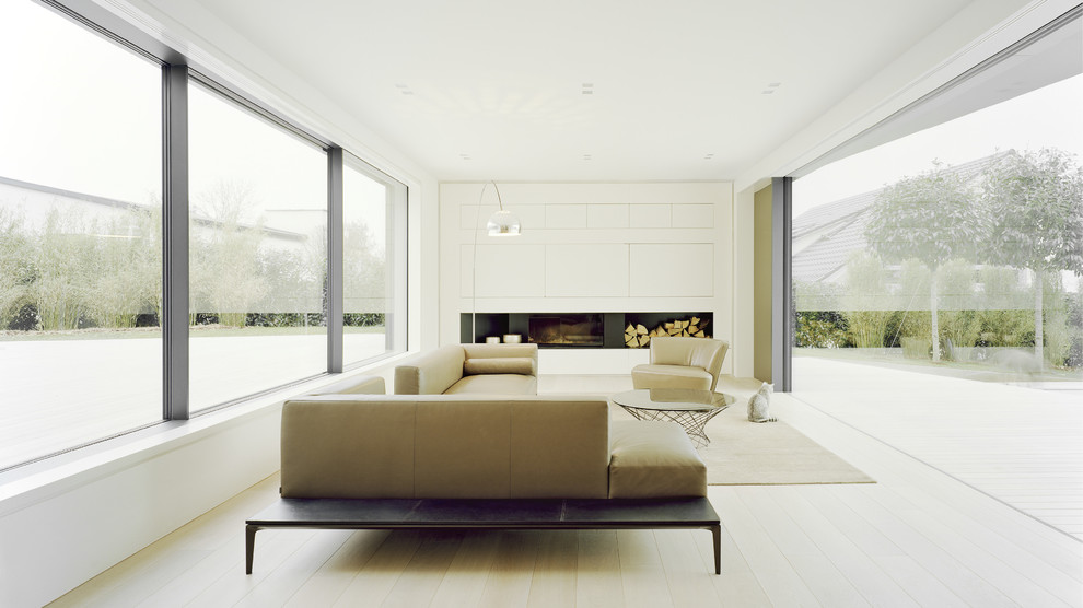 Immagine di un grande soggiorno minimal aperto con pareti bianche, parquet chiaro, camino classico, cornice del camino in intonaco e TV nascosta