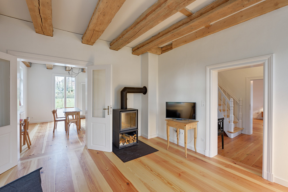 Diseño de salón cerrado clásico con paredes blancas, suelo de madera en tonos medios, estufa de leña y televisor independiente
