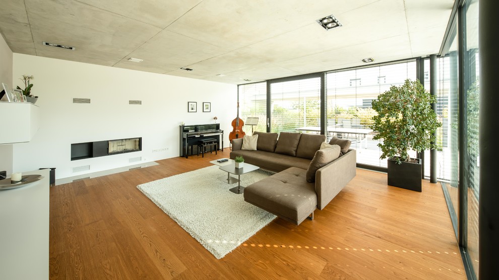 Modelo de salón con rincón musical minimalista de tamaño medio con suelo de madera clara, todas las chimeneas, marco de chimenea de yeso, paredes blancas y suelo marrón