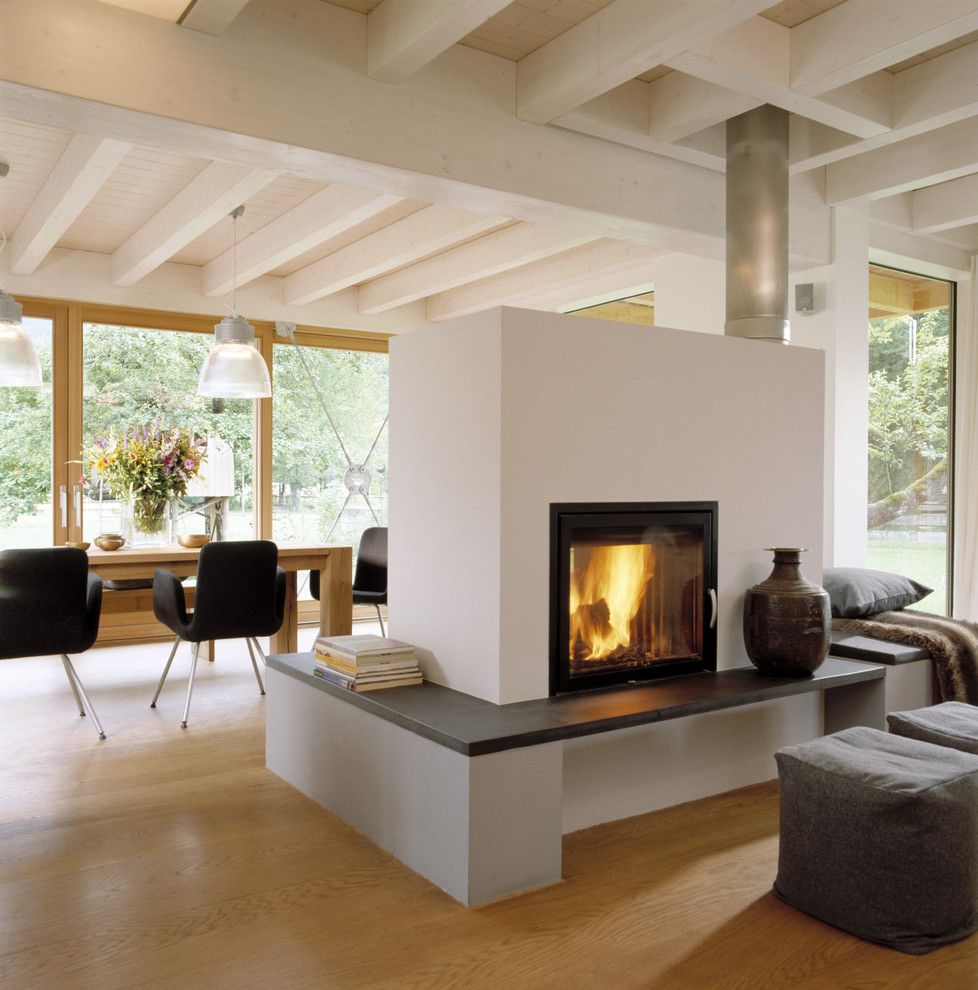 Cette photo montre un salon tendance ouvert avec un mur blanc, parquet clair, une cheminée double-face et un manteau de cheminée en plâtre.